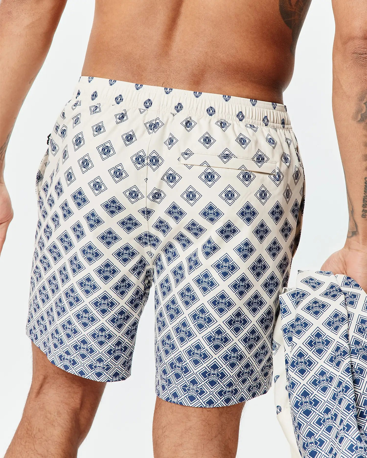 Mens Tobias Swim Trunk in cream with a navy blue all-over geometric pattern featuring the small Psycho Bunny skull logo, classic fit, smooth quick-dry fabric, and a back pocket.