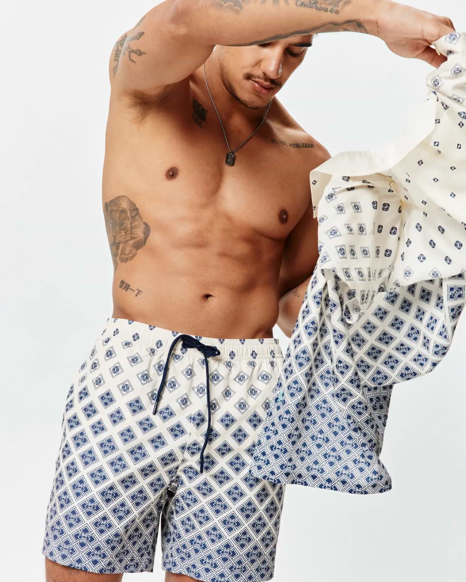 Mens Tobias Swim Trunk in cream with a navy blue geometric pattern featuring the Psycho Bunny skull logo, classic fit, smooth quick-dry fabric, and a navy drawstring.