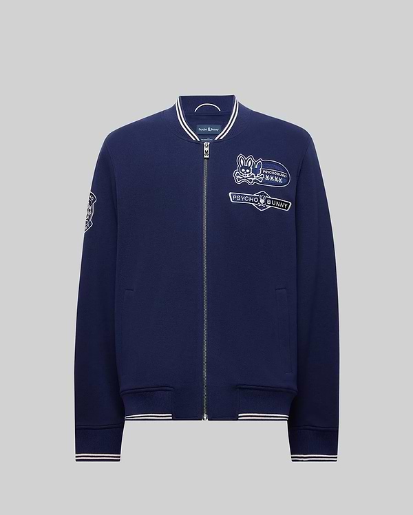 The Psycho Bunny MENS DESMOND PIQUE KNIT BOMBER (MO1100018) is a navy varsity zip-up jacket with white-trimmed collar, cuffs, and hem, embroidered cartoon bunny and "PSYCHO BUNNY" on the chest, plus sleeve designs. (6)