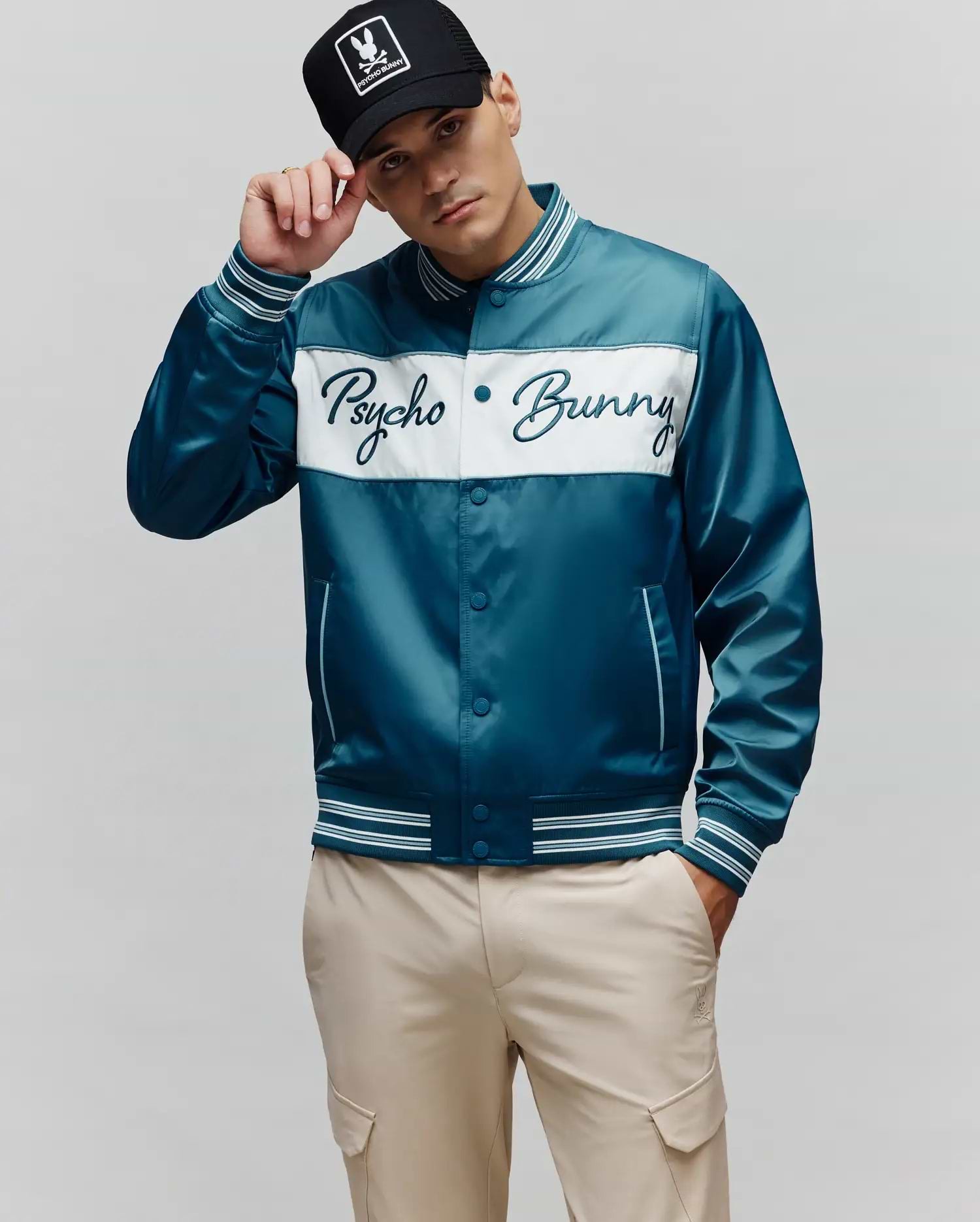 Mens Thomas Satin Bomber in teal with a white chest panel featuring an embroidered Psycho Bunny script logo, classic fit, and striped ribbed trim.