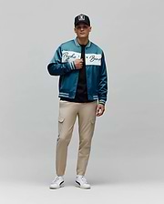Mens Thomas Satin Bomber in teal, featuring a glossy satin texture, a prominent white chest stripe with a large Psycho Bunny script logo, and striped ribbed cuffs, collar, and hem for a classic fit.