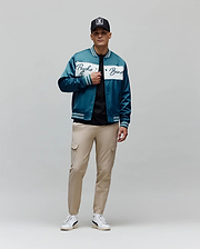 Mens Thomas Satin Bomber in teal, featuring a glossy satin texture, a prominent white chest stripe with a large Psycho Bunny script logo, and striped ribbed cuffs, collar, and hem for a classic fit.