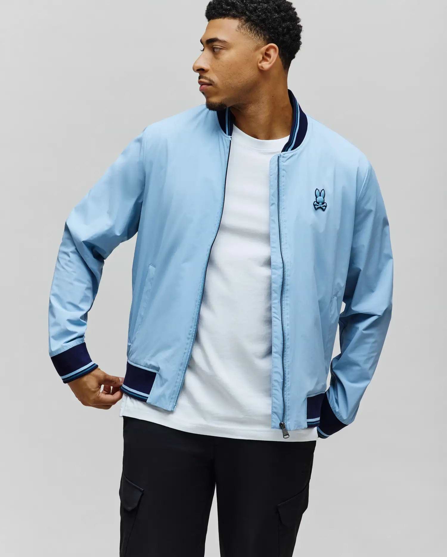 Light blue Mens Aldrin Bomber, classic fit, with navy and light blue striped ribbed collar, cuffs, and hem. Features a small embroidered light blue Psycho Bunny skull logo on the left chest. (1)