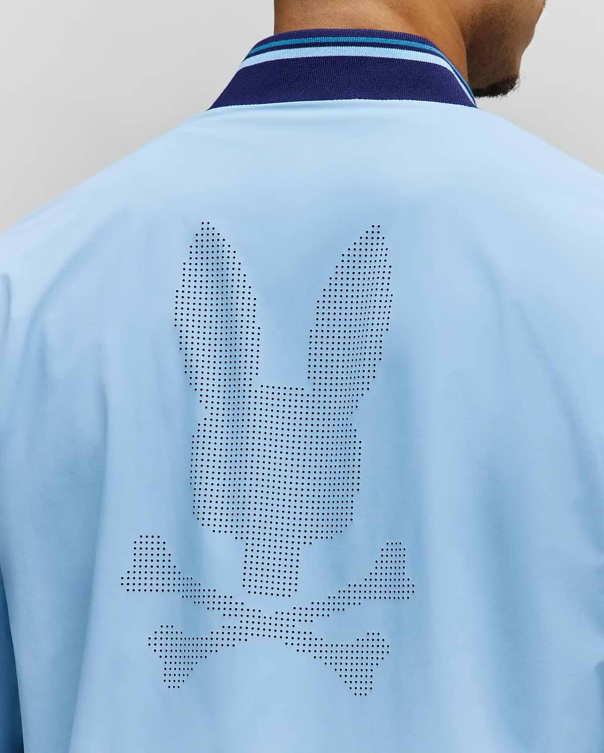 Mens Aldrin Bomber in sky blue, featuring a large perforated Psycho Bunny skull logo centered on the back. It has a smooth fabric and a navy and light blue striped ribbed collar. (4)