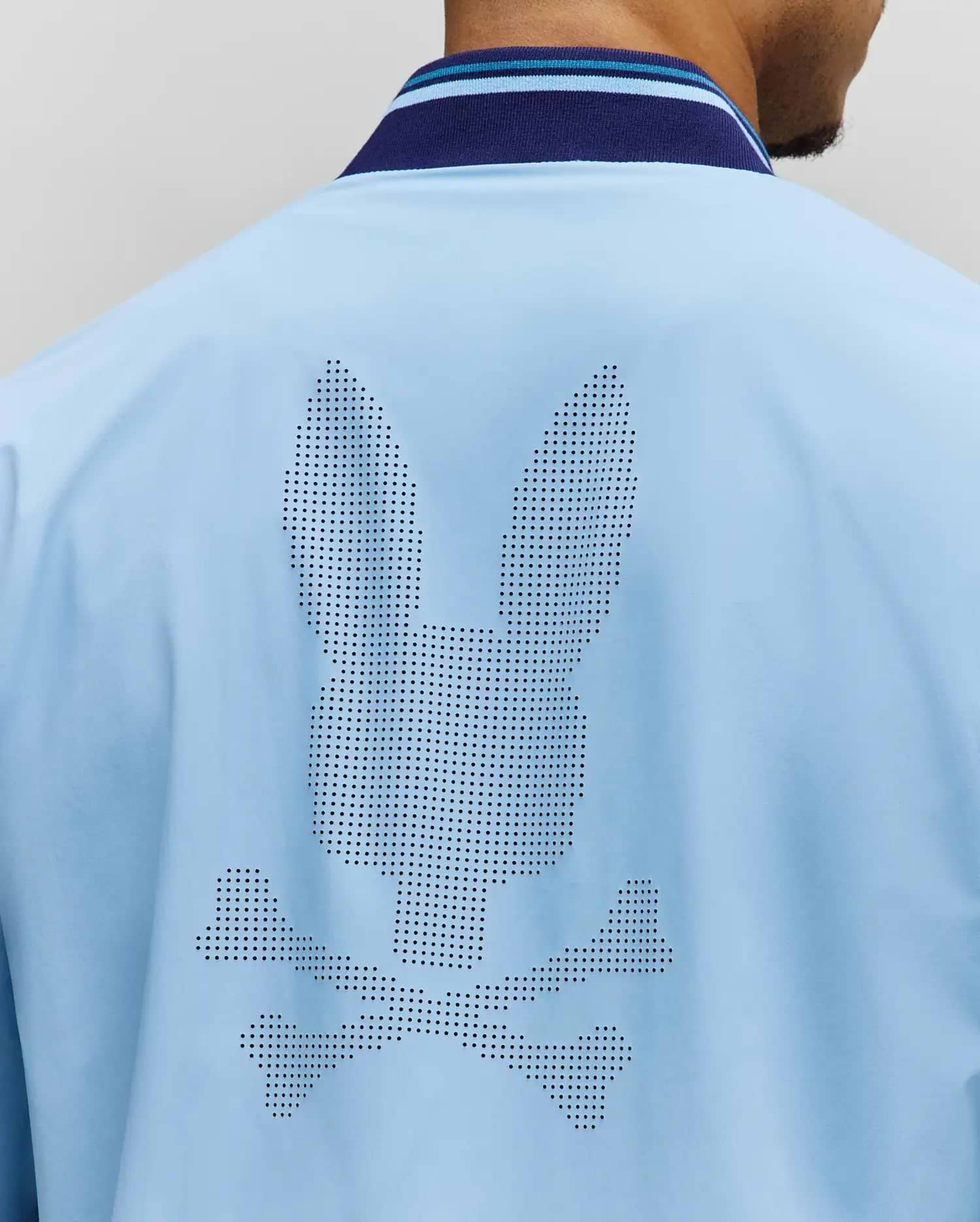Mens Aldrin Bomber in sky blue, featuring a large perforated Psycho Bunny skull logo centered on the back. It has a smooth fabric and a navy and light blue striped ribbed collar. (4)