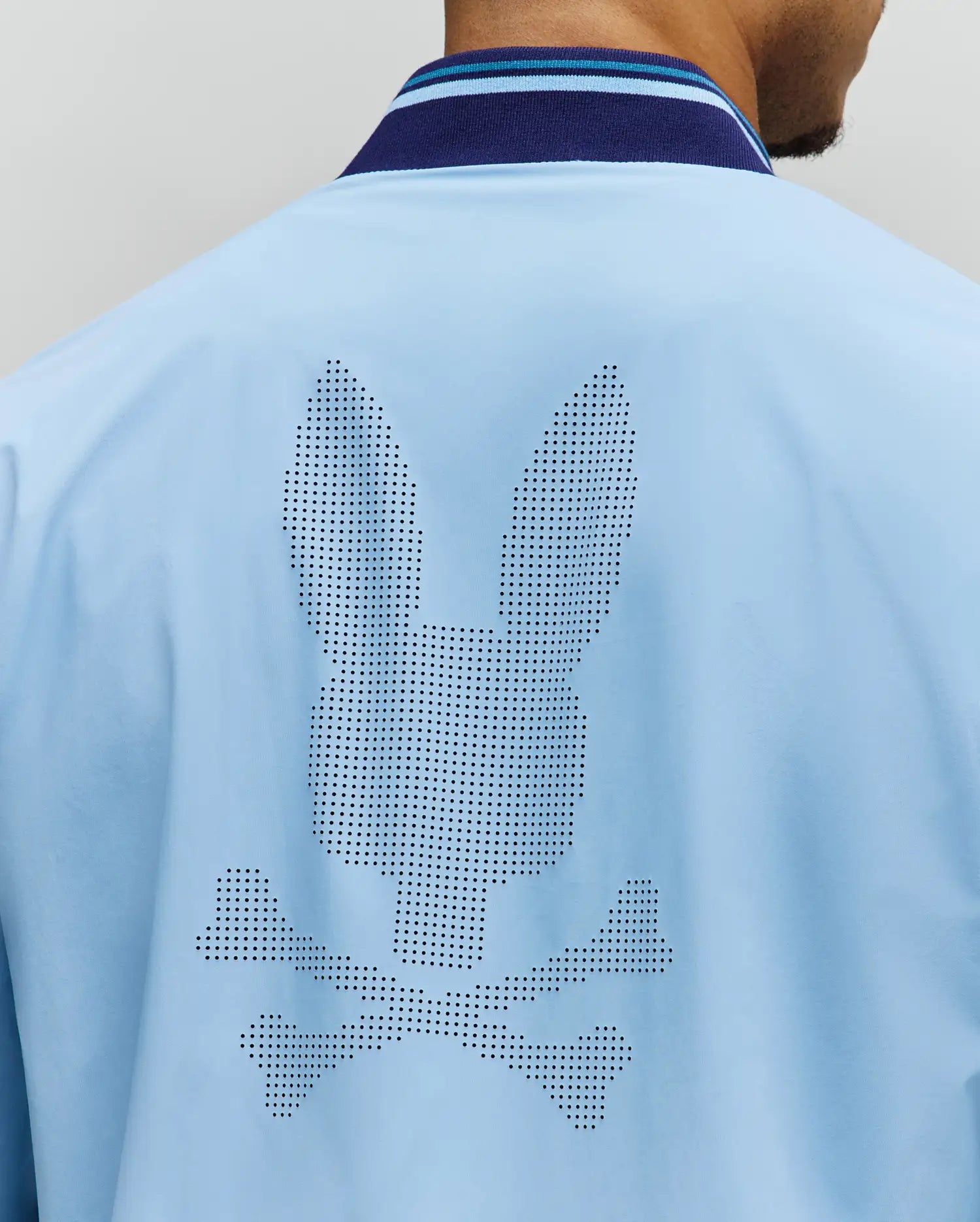 Mens Aldrin Bomber in sky blue, featuring a large perforated Psycho Bunny skull logo centered on the back. It has a smooth fabric and a navy and light blue striped ribbed collar. (4)