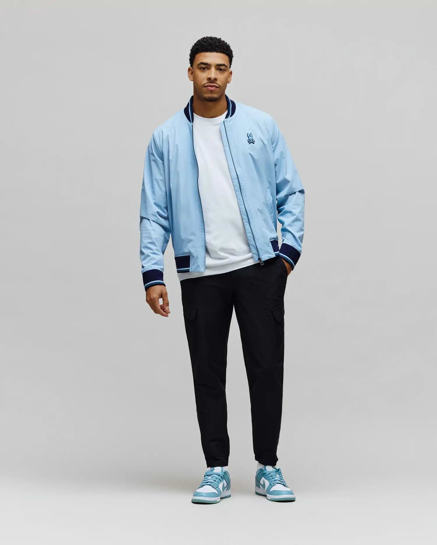 Sky Blue Mens Aldrin Bomber jacket, relaxed fit, with navy/white striped ribbed collar, cuffs, hem, and an embroidered Psycho Bunny skull logo on the left chest. (6)