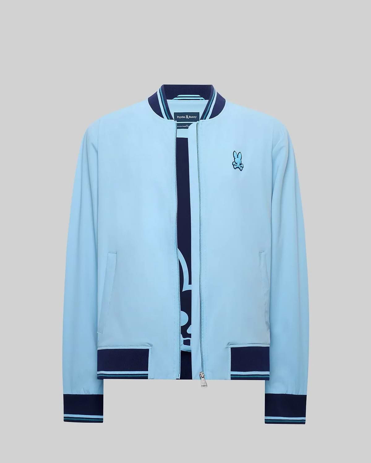 Mens Aldrin Bomber sky blue jacket, classic fit, with navy blue ribbed collar, cuffs, and hem featuring light blue stripes. Full zip closure and an embroidered Psycho Bunny skull logo on the left chest. (7)