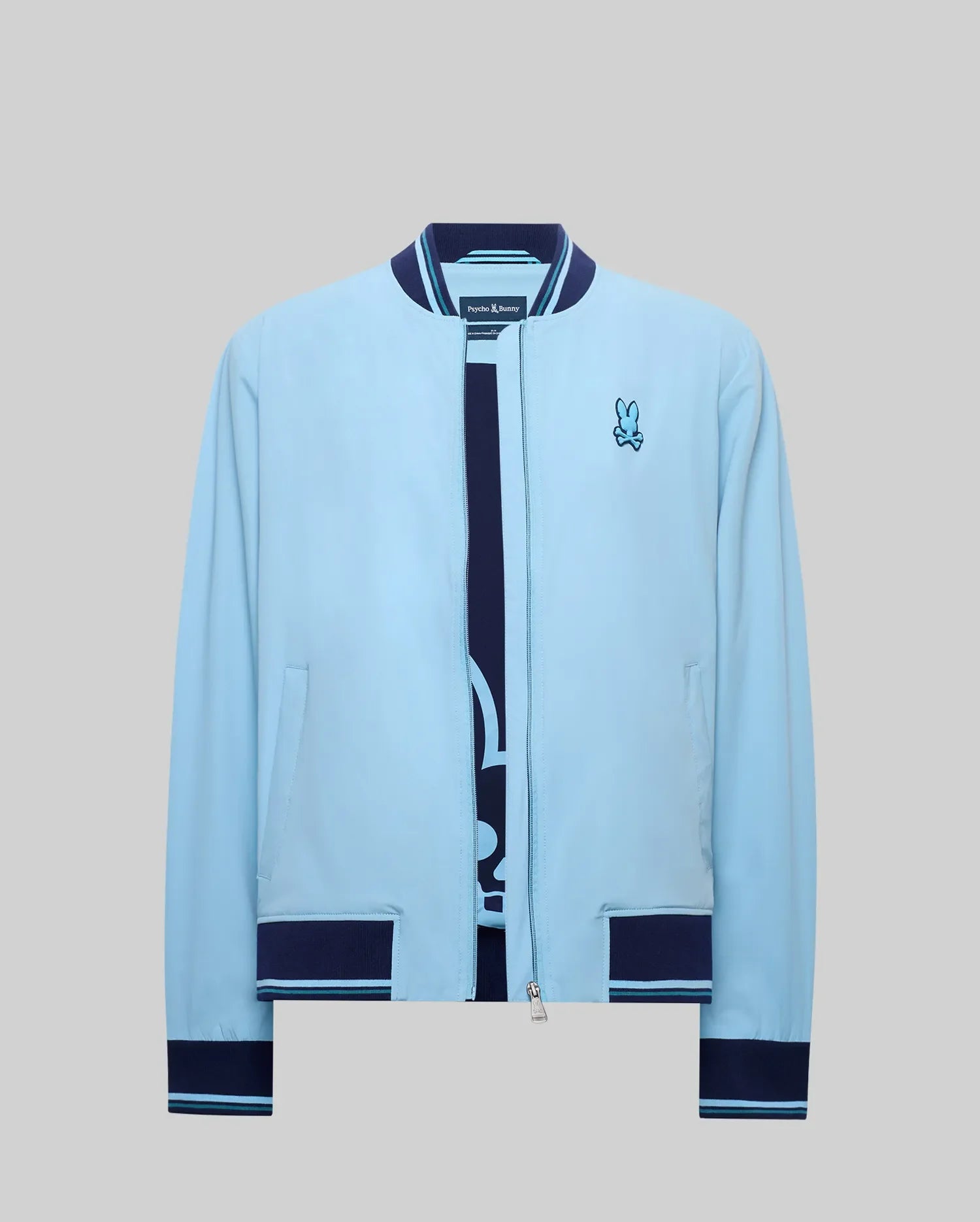 Mens Aldrin Bomber sky blue jacket, classic fit, with navy blue ribbed collar, cuffs, and hem featuring light blue stripes. Full zip closure and an embroidered Psycho Bunny skull logo on the left chest. (7)