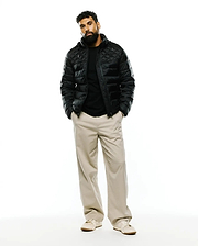 Black Mens Emerik Hooded Puffer Jacket with a classic fit, featuring diamond quilting and a shiny finish. Paired with a black jersey t-shirt and relaxed khaki wide-leg pants.