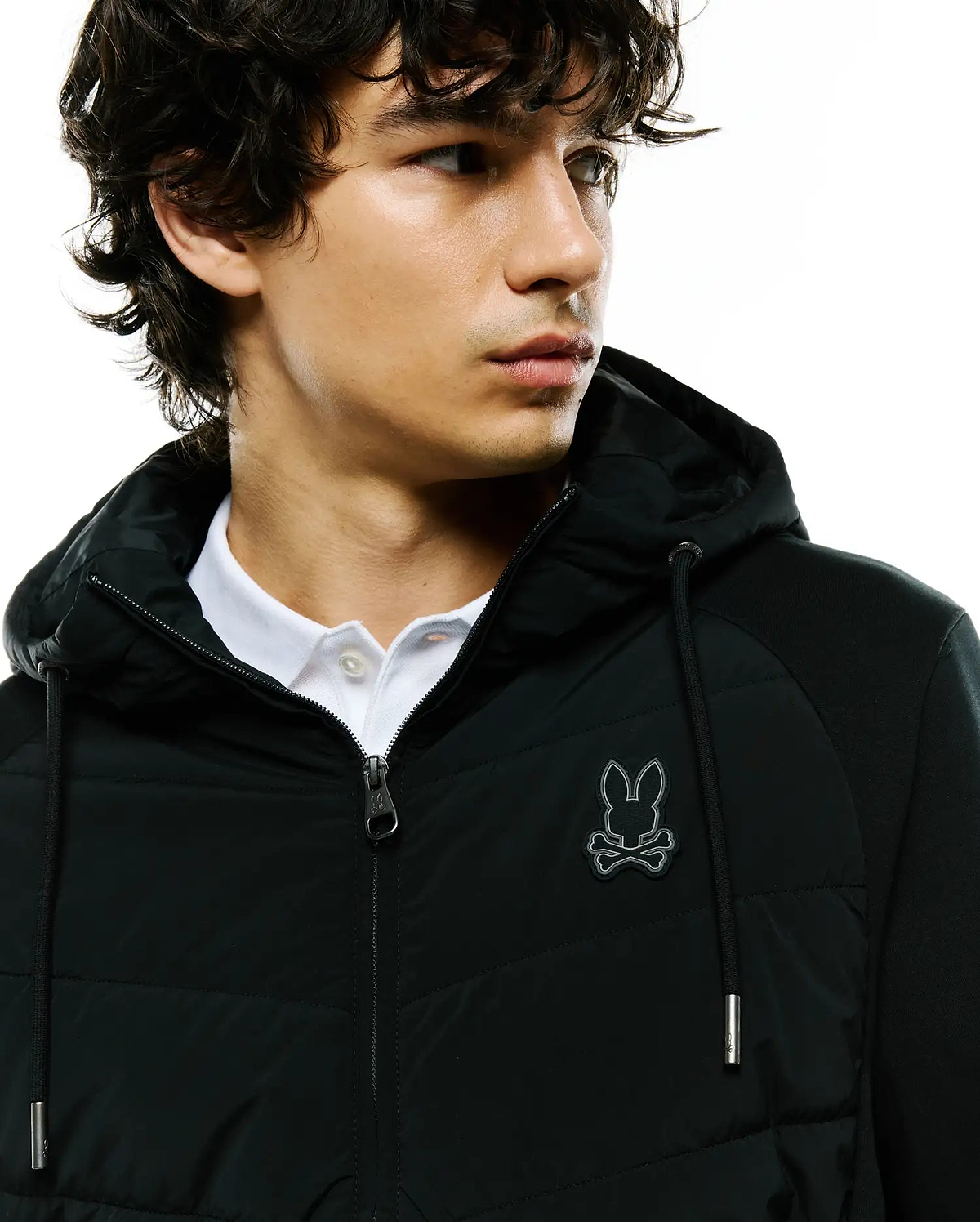 Mens Gordley Mix Media Jacket: Black hooded full-zip jacket with a quilted front panel, knit sleeves, and an embroidered silver-outlined Psycho Bunny skull logo on the left chest, featuring a classic fit and silver hardware.