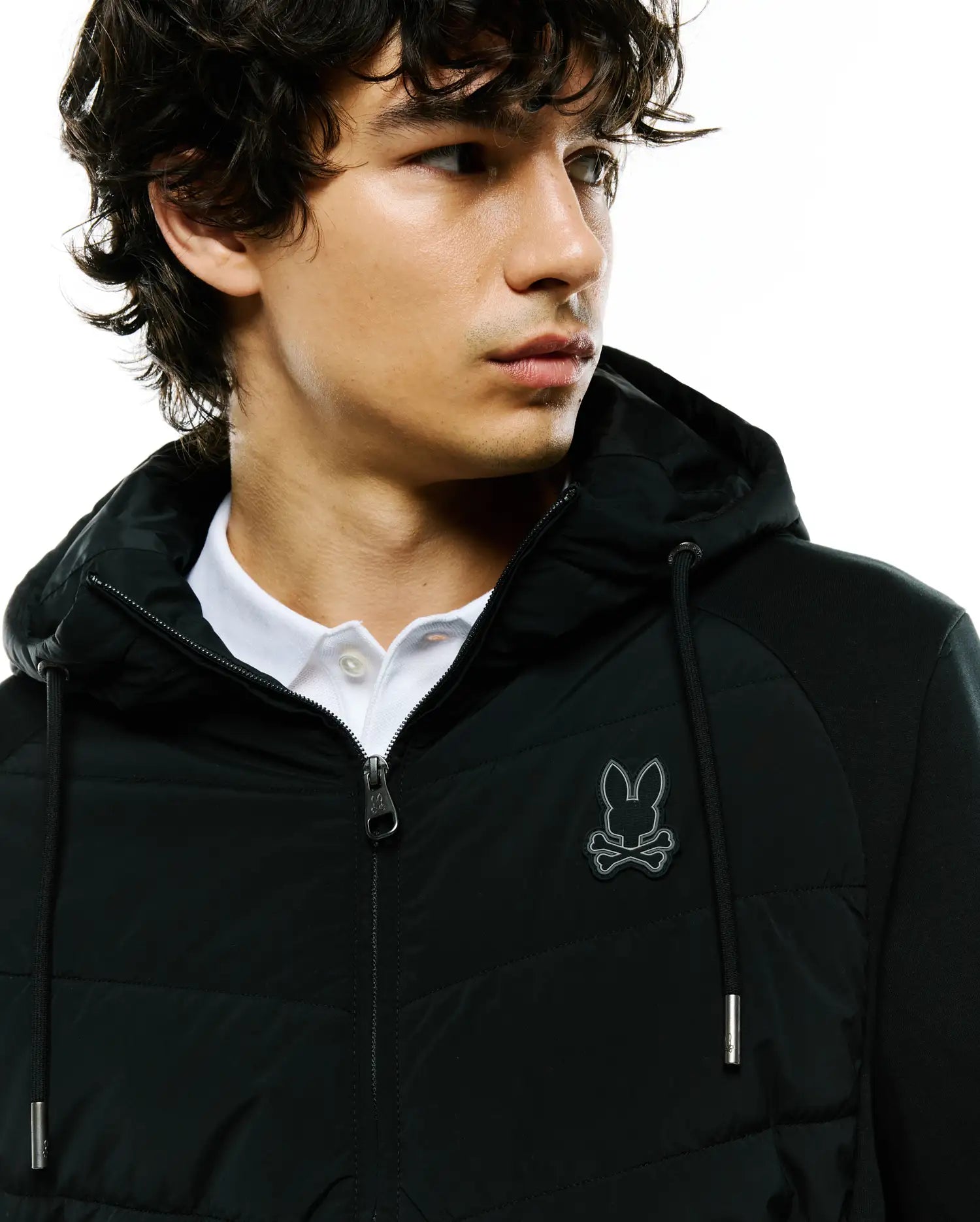 Mens Gordley Mix Media Jacket: Black hooded full-zip jacket with a quilted front panel, knit sleeves, and an embroidered silver-outlined Psycho Bunny skull logo on the left chest, featuring a classic fit and silver hardware.