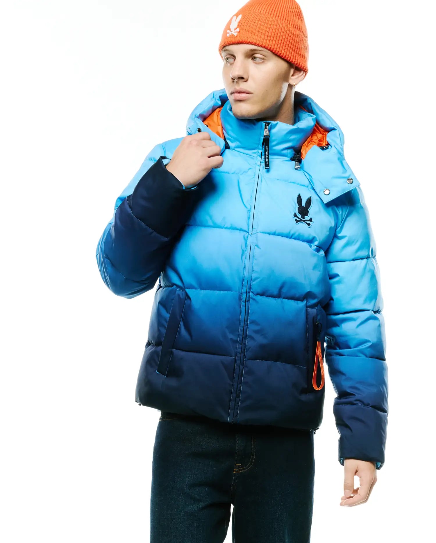 Men's Solan Puffer Jacket, an ombre blue quilted puffer jacket with a hooded design, featuring a black Psycho Bunny skull logo on the left chest and bright orange lining accents. (1)