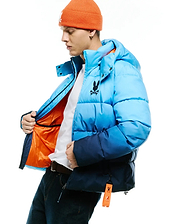 Men's Solan Puffer Jacket, an ombre light to dark blue padded jacket with a navy bottom, features a large black embroidered Psycho Bunny skull logo on the left chest, bright orange lining, and a branded orange tag. (3)