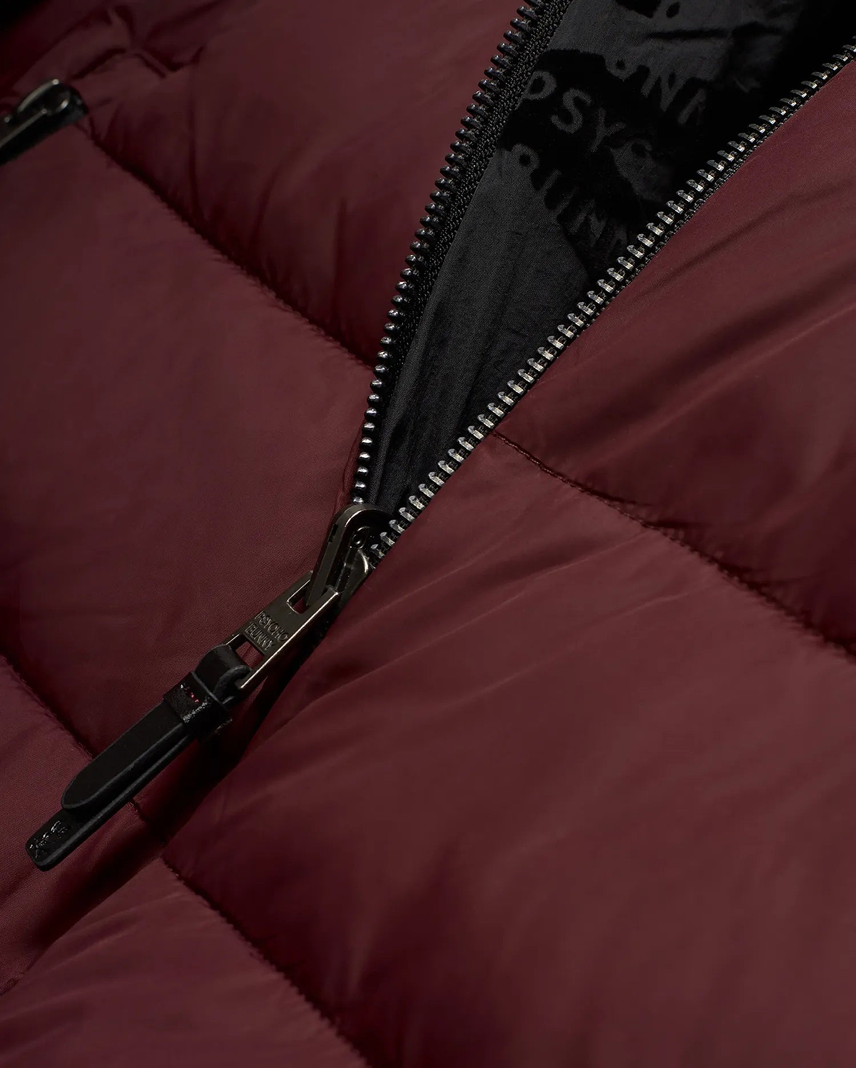 Men's Angus Reversible Bomber in deep maroon, featuring a padded, quilted texture, black full-zip closure with a Psycho Bunny branded pull, and a black inner lining with a repeating Psycho Bunny text pattern. (6)