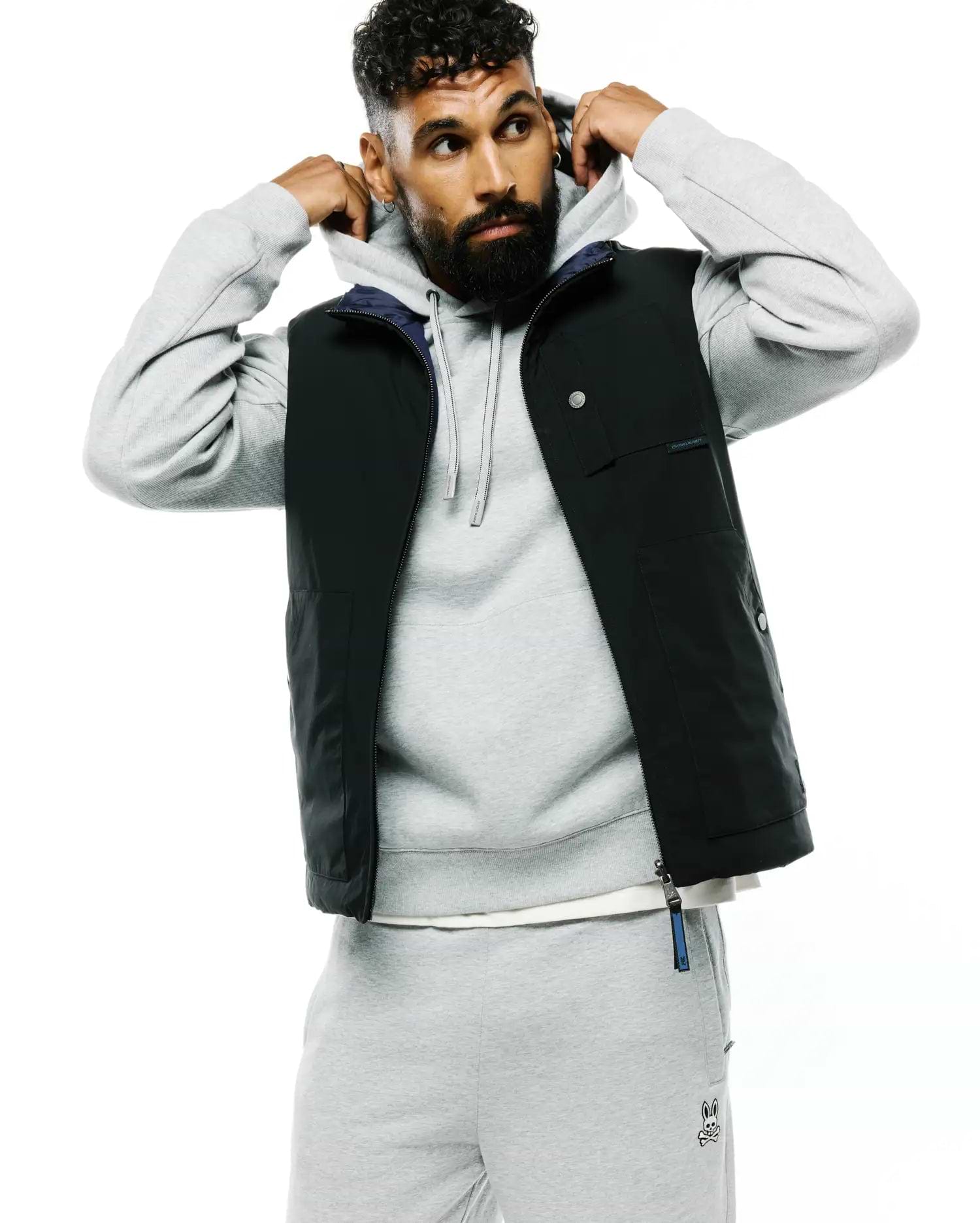 Mens Gordler Reversible Vest, a classic fit black vest with a smooth finish, featuring a navy interior, full zip, snap-button chest pockets, and a Psycho Bunny text label on the chest with a branded zipper pull.