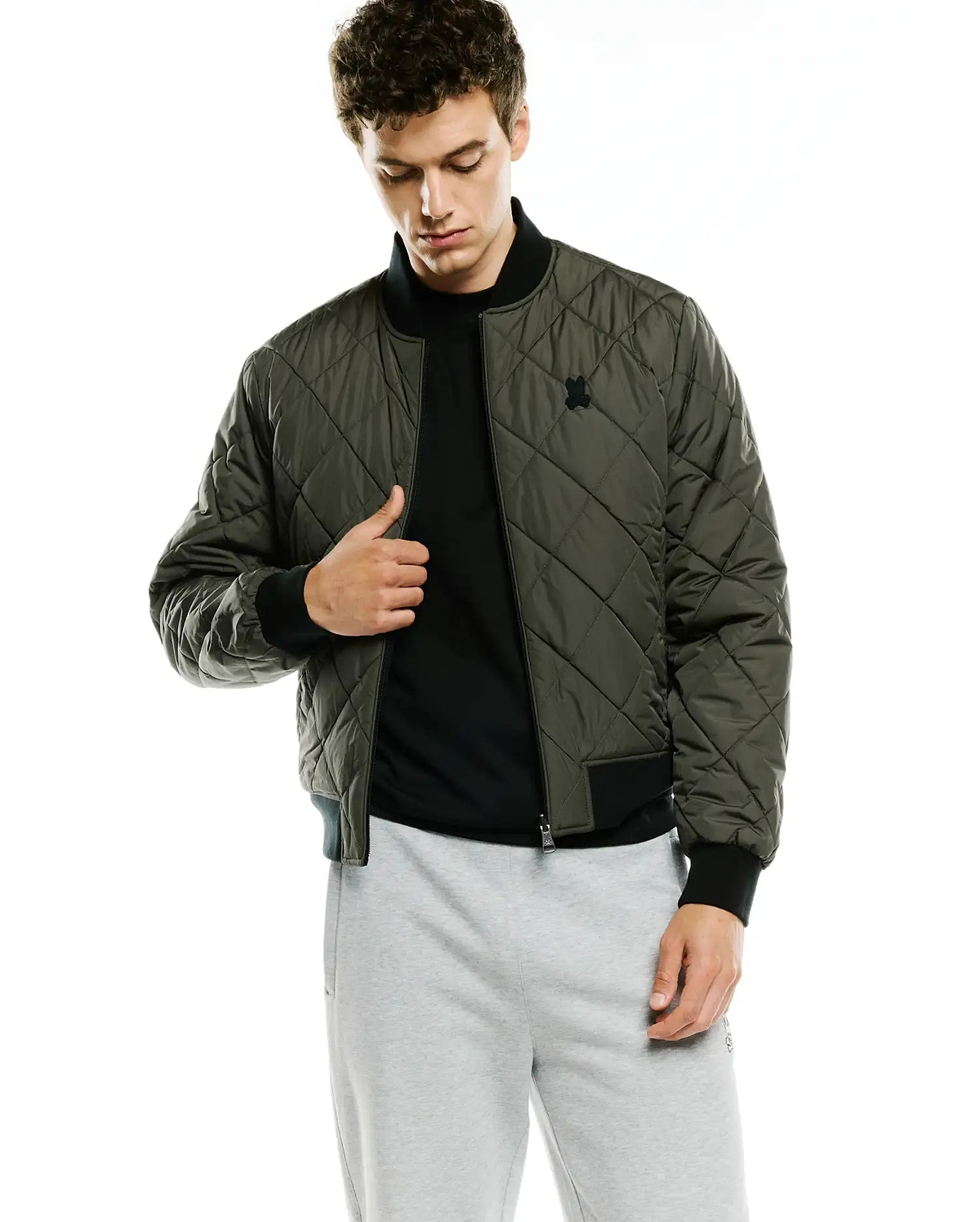 Mens Joaquin Mix Media Reversible Bomber in olive green with diamond quilting, black ribbed collar, cuffs, and hem, featuring a small black embroidered Psycho Bunny skull logo on the left chest.
