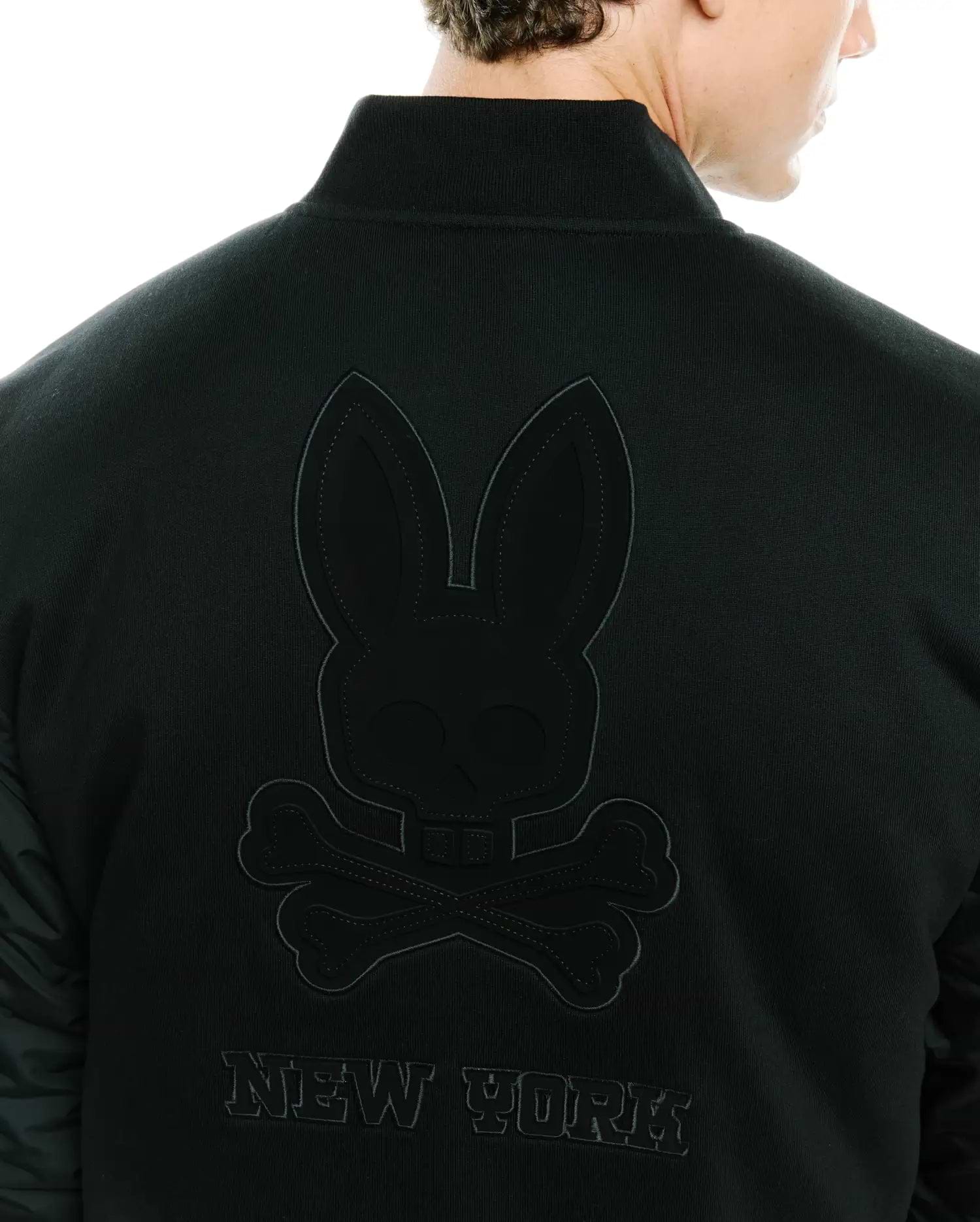 Mens Joaquin Mix Media Reversible Bomber in black, featuring a large tonal embroidered Psycho Bunny skull logo and NEW YORK text on the back, with contrasting quilted sleeves.