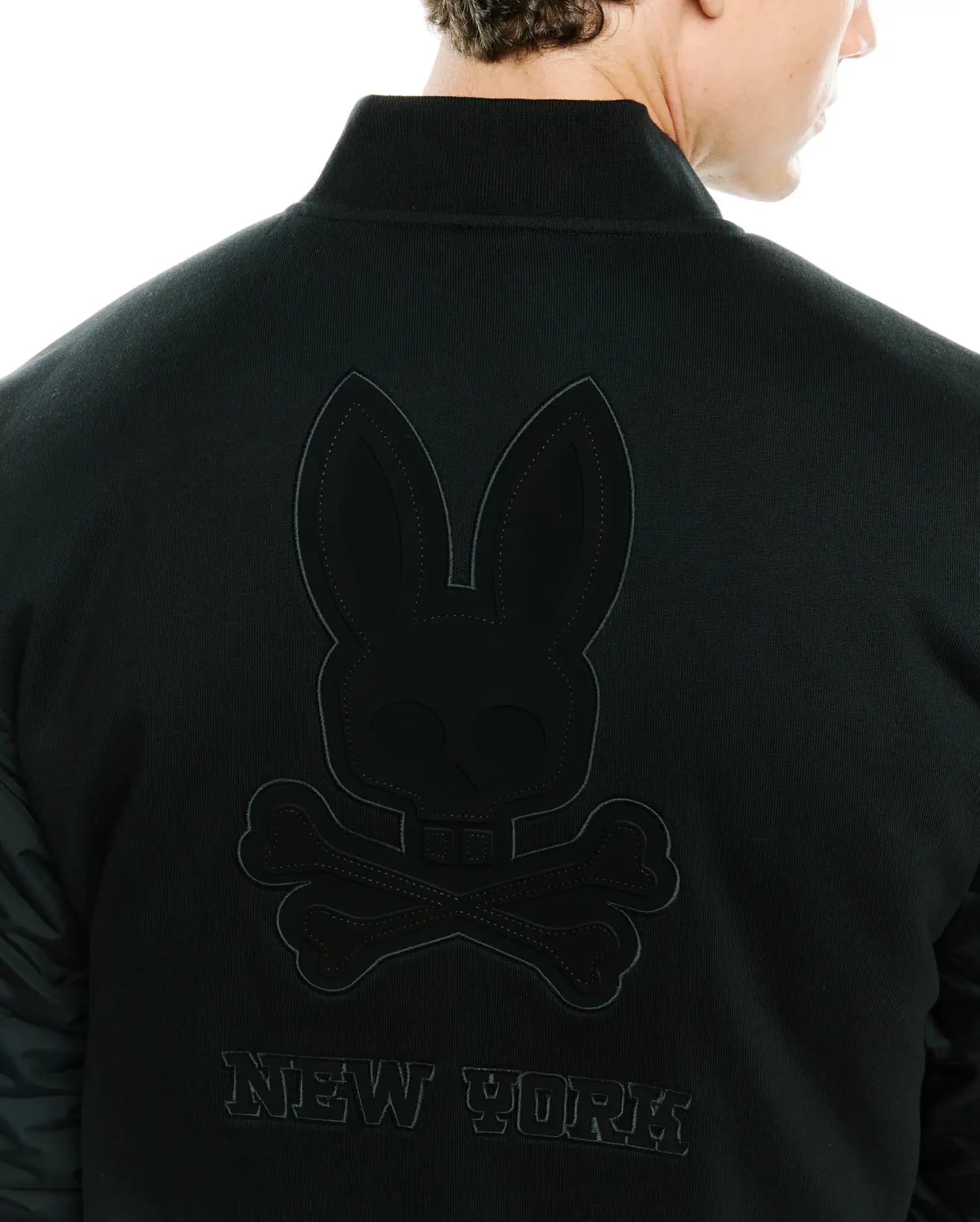 Mens Joaquin Mix Media Reversible Bomber in black, featuring a large tonal embroidered Psycho Bunny skull logo and NEW YORK text on the back, with contrasting quilted sleeves.