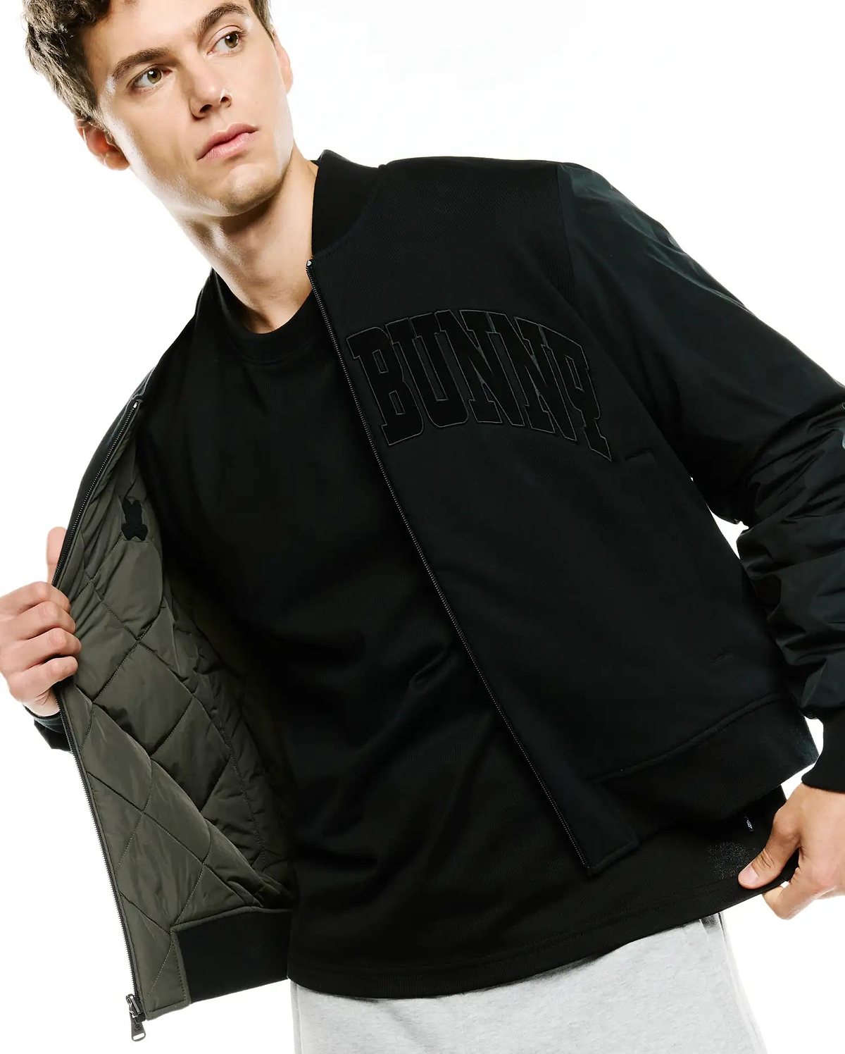 Black Mens Joaquin Mix Media Reversible Bomber jacket with large embroidered BUNNY text on chest, smooth outer fabric, and olive green quilted lining featuring a small Psycho Bunny skull logo.