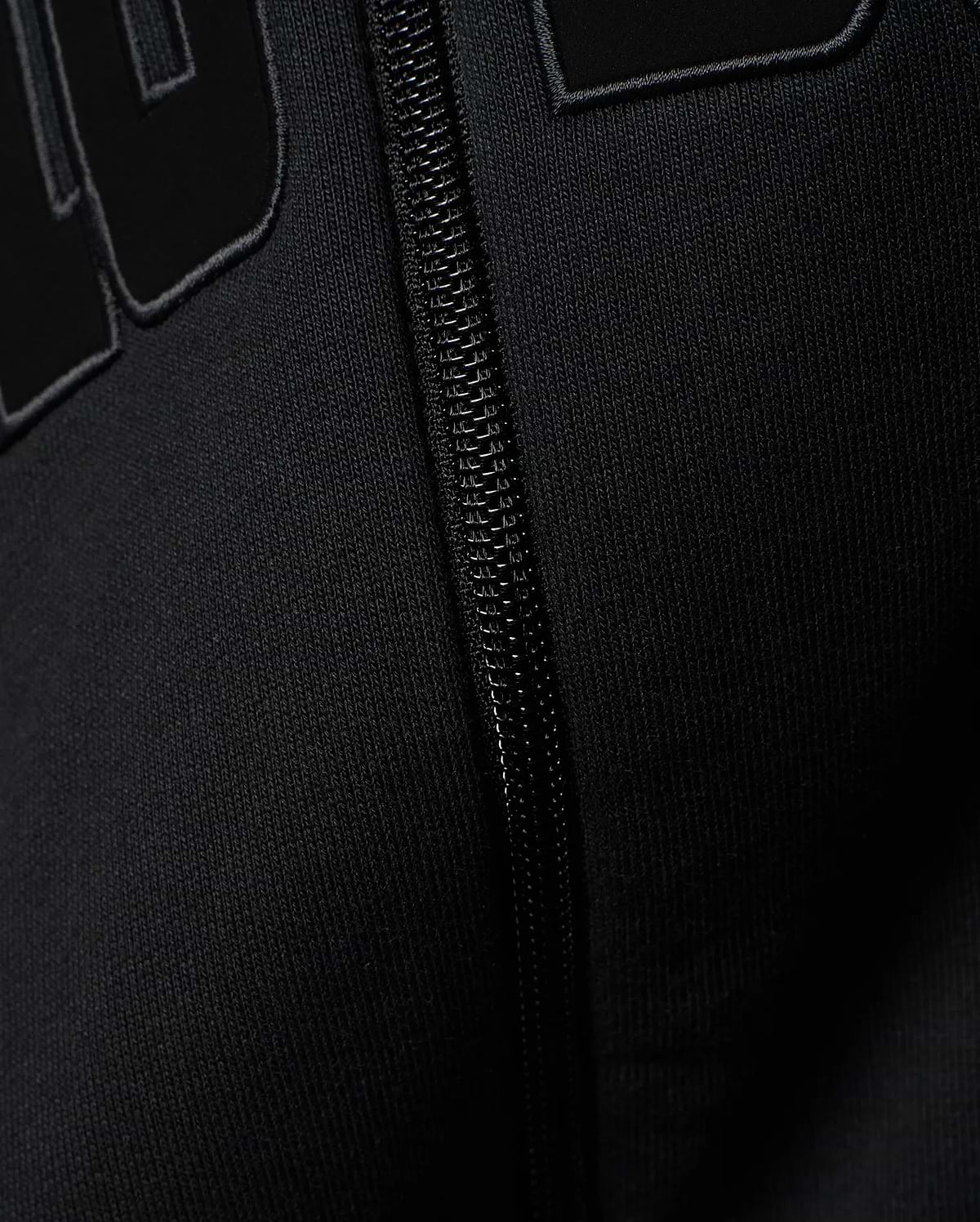 Mens Joaquin Mix Media Reversible Bomber in black, showcasing large raised black letters with a subtle grey outline on a smooth knit fabric, alongside a black front zipper.
