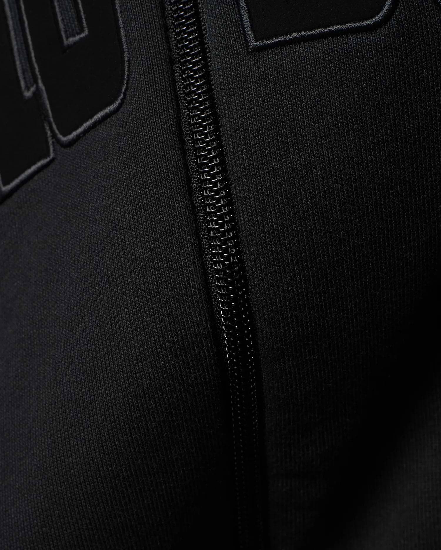 Mens Joaquin Mix Media Reversible Bomber in black, showcasing large raised black letters with a subtle grey outline on a smooth knit fabric, alongside a black front zipper.