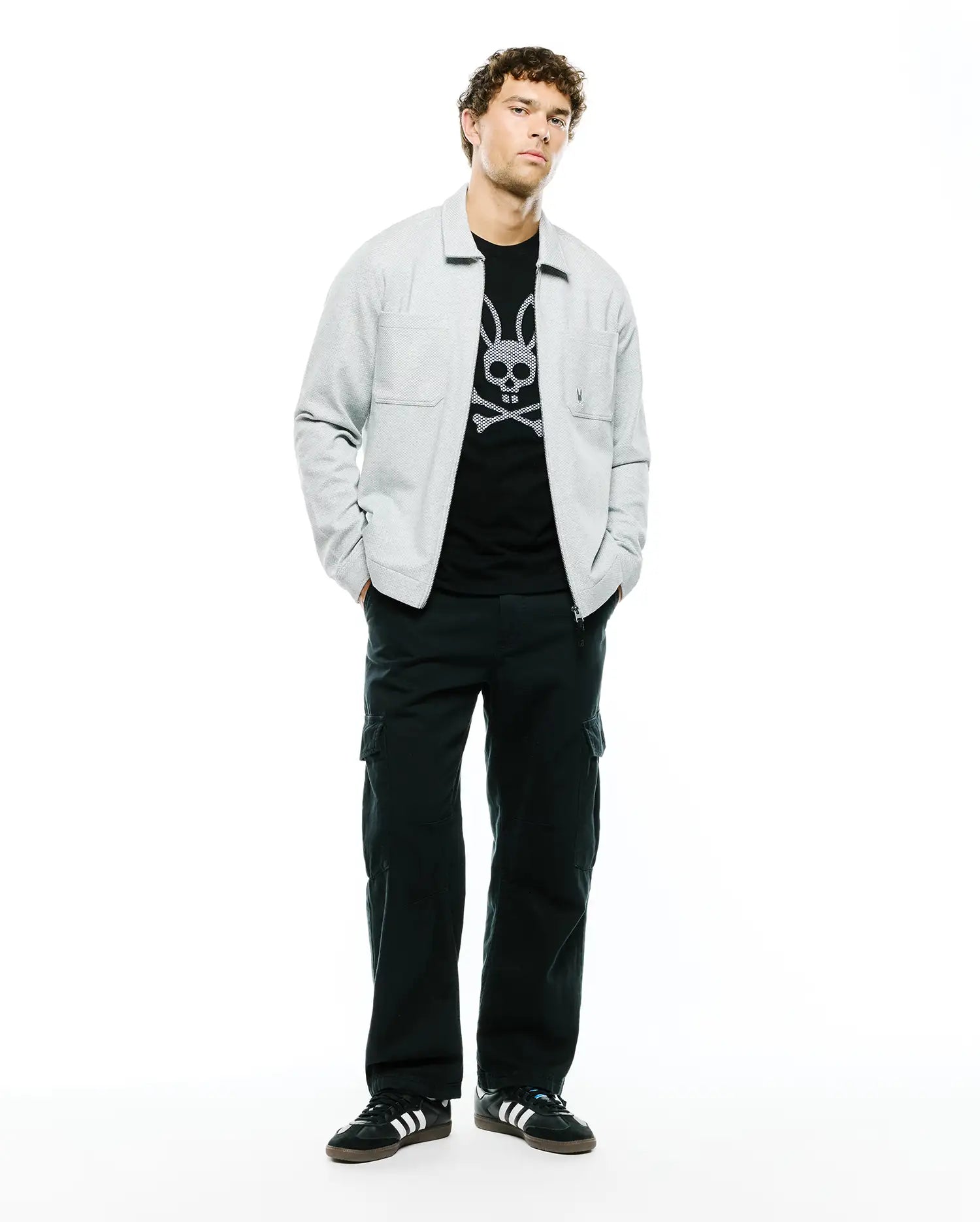 Mens Marc Textured Overshirt in light grey, featuring a subtle textured fabric, classic collar, and a single chest pocket, worn over a black t-shirt with a large white Psycho Bunny skull and crossbones graphic.