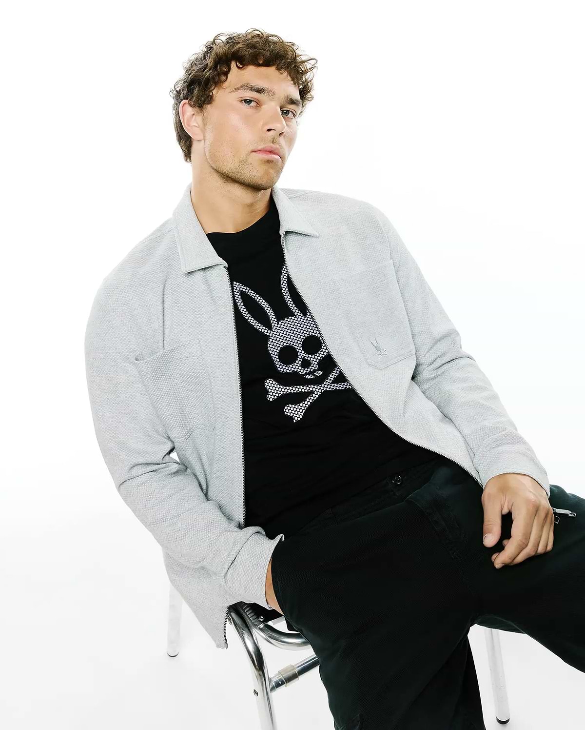 Mens Marc Textured Overshirt in light grey, featuring a full zip, collared design, and small embroidered Psycho Bunny logo on the chest pocket, layered over a black jersey t-shirt with a large white bunny skull graphic.