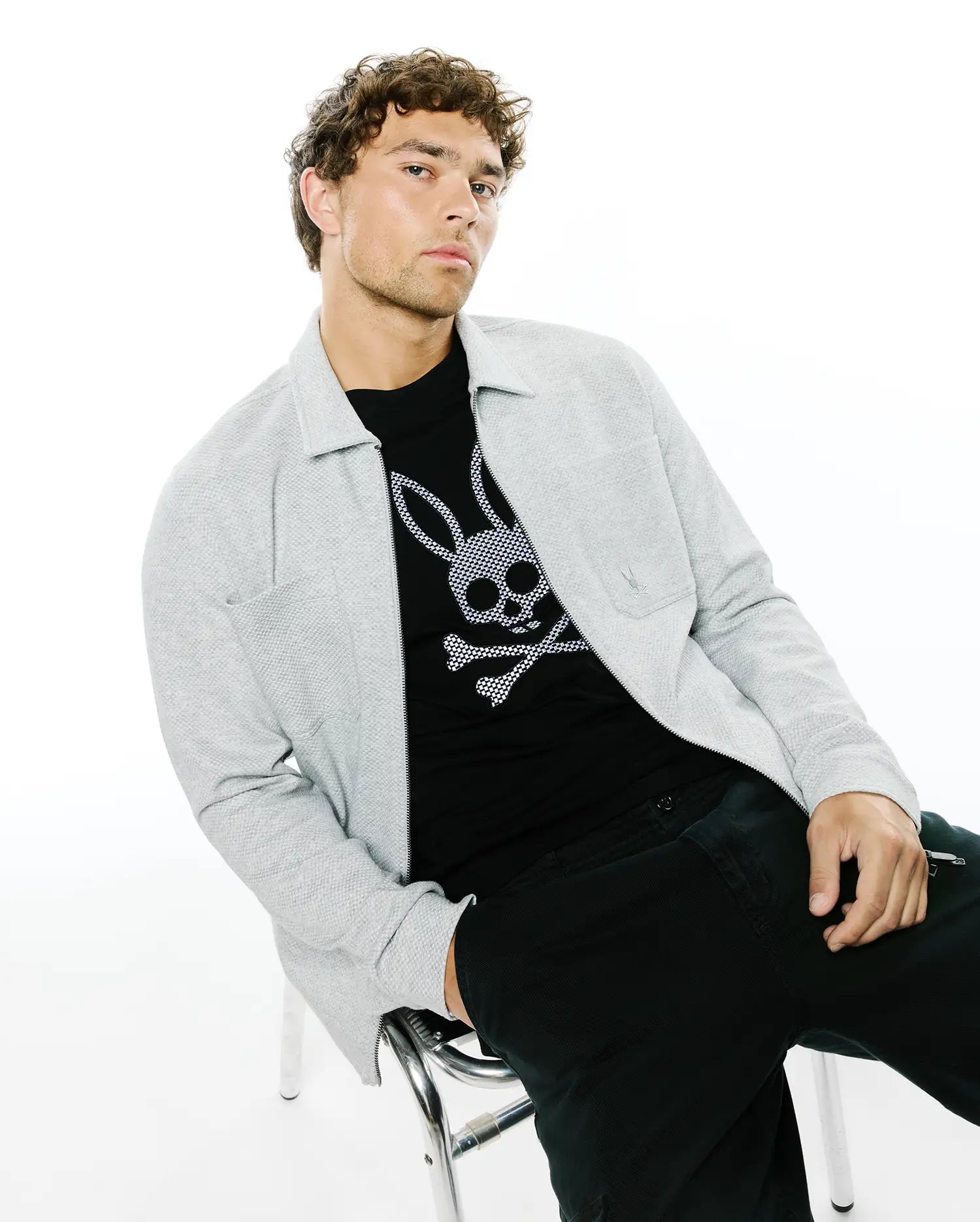 Mens Marc Textured Overshirt in light grey, featuring a full zip, collared design, and small embroidered Psycho Bunny logo on the chest pocket, layered over a black jersey t-shirt with a large white bunny skull graphic.