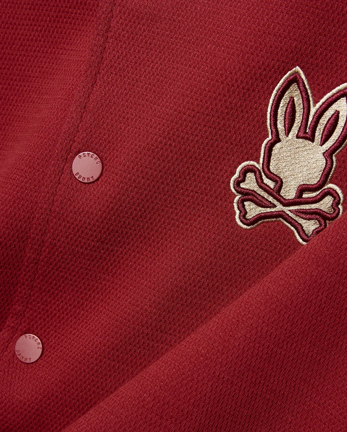 Mens Reilly Knit Bomber in deep red pique knit, featuring a large embroidered gold and burgundy Psycho Bunny skull logo on the chest and matching branded buttons. (5)