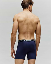 A shirtless man is shown from the back wearing navy blue Psycho Bunny MENS 3 PACK BOXER BRIEF - MO1400006, featuring a black waistband with "PSYCHO BUNNY" text and bunny logos in white. The plain light background highlights all-day comfort.