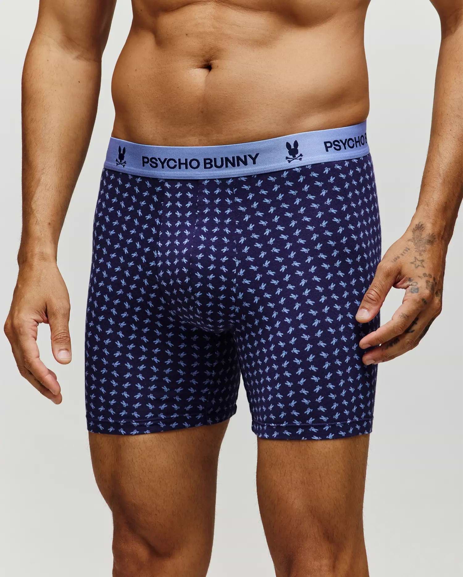 A man models the Psycho Bunny MENS SINGLE BOXER BRIEF - MO1400010 in navy, featuring a light blue waistband with the brand name and a soft Pima cotton fabric adorned with a repeating light blue bunny pattern for all-day comfort. (2)