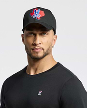A man dons Psycho Bunny's MENS TEXAS BASEBALL CAP - MO1500014 with a colorful logo and a black cotton shirt embellished with a small design, set against a plain white background. (6)