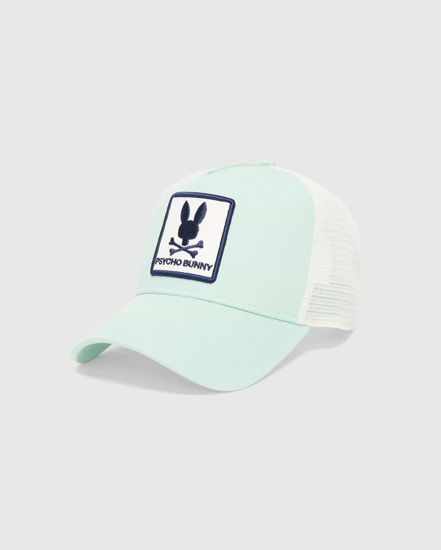 MENS ADAMO TRUCKER CAP in mint green cotton twill with white mesh back, featuring a large front embroidered patch with the navy blue Psycho Bunny skull logo and text on a white background.
