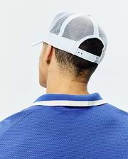 White Mens Adamo Trucker Cap with mesh back and snap closure, paired with a royal blue pique polo shirt featuring a blue and white striped collar.