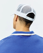 White Mens Adamo Trucker Cap with mesh back and snap closure, paired with a royal blue pique polo shirt featuring a blue and white striped collar.