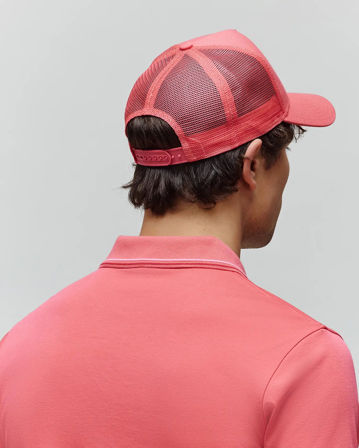 Vibrant coral pink Mens Ara Trucker Cap featuring a breathable mesh back and adjustable snapback closure, paired with a matching coral pink polo shirt with a refined ribbed collar accented by a thin white stripe. (3)
