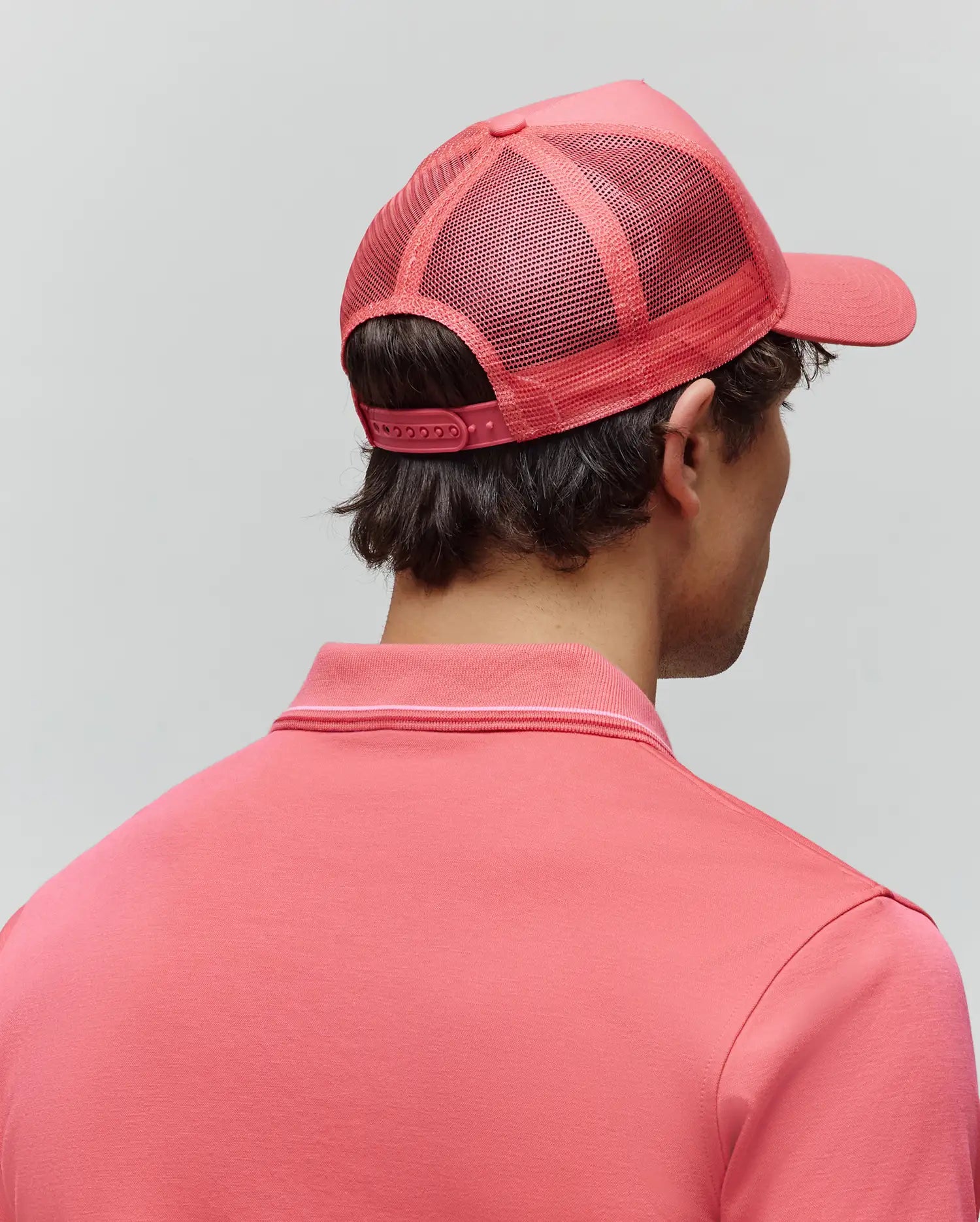 Vibrant coral pink Mens Ara Trucker Cap featuring a breathable mesh back and adjustable snapback closure, paired with a matching coral pink polo shirt with a refined ribbed collar accented by a thin white stripe. (3)