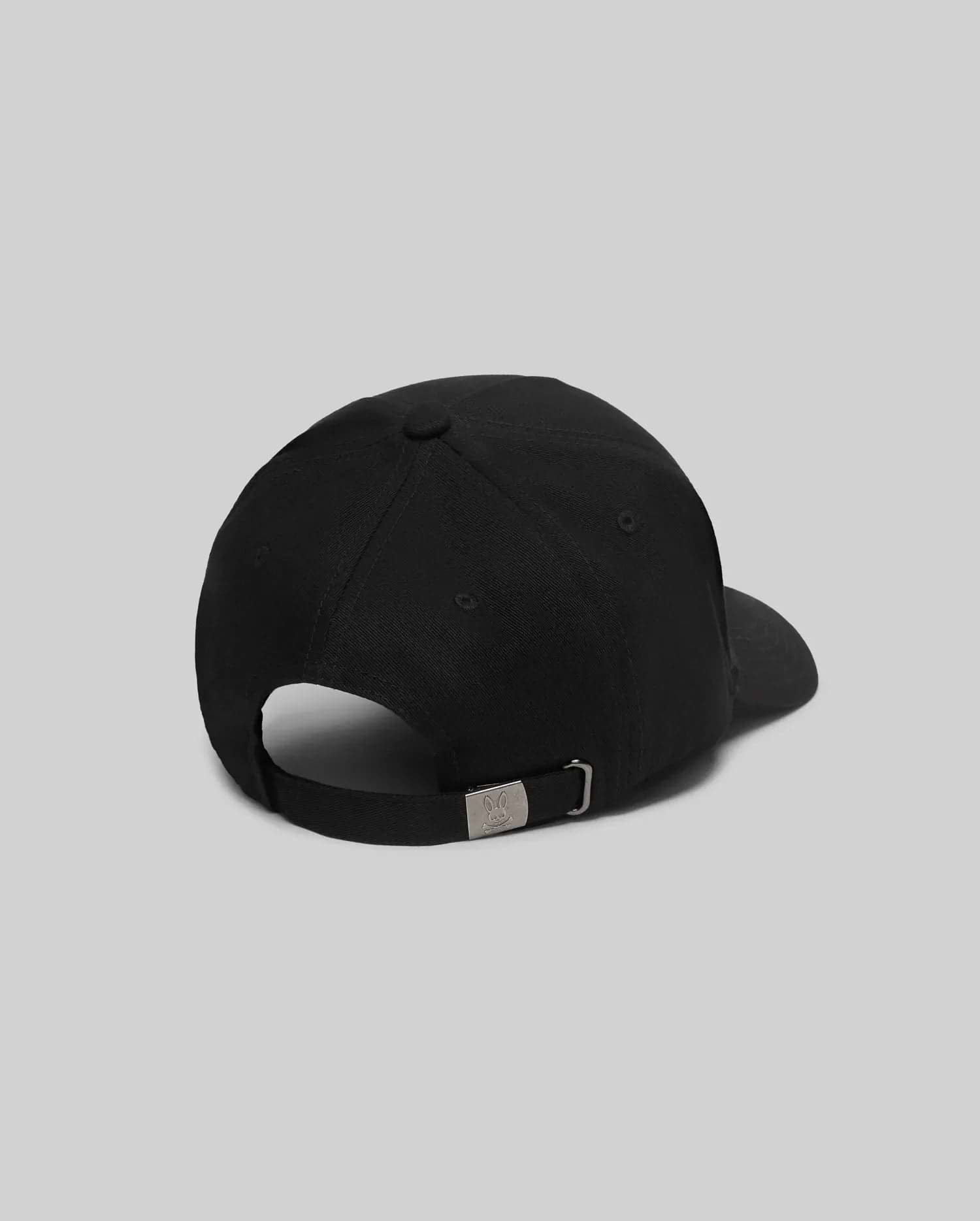 Mens Oscar Trucker Cap, a sleek black baseball cap with a smooth fabric finish and an adjustable back strap featuring a gunmetal buckle engraved with the iconic Psycho Bunny skull logo.