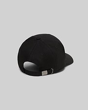 Mens Oscar Trucker Cap, a sleek black baseball cap with a smooth fabric finish and an adjustable back strap featuring a gunmetal buckle engraved with the iconic Psycho Bunny skull logo.