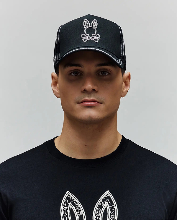 Black Mens Oscar Trucker Cap with white contrast stitching and an embroidered white and pink Psycho Bunny skull logo. Paired with a black jersey t-shirt featuring a large white graphic print.
