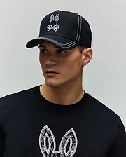 Black Mens Oscar Trucker Cap with white embroidered Psycho Bunny skull logo and white contrast stitching, paired with a black jersey t-shirt featuring a large white patterned Psycho Bunny ear graphic on the chest. (5)
