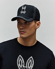 Black Mens Oscar Trucker Cap with white embroidered Psycho Bunny skull logo and white contrast stitching, paired with a black jersey t-shirt featuring a large white patterned Psycho Bunny ear graphic on the chest. (5)
