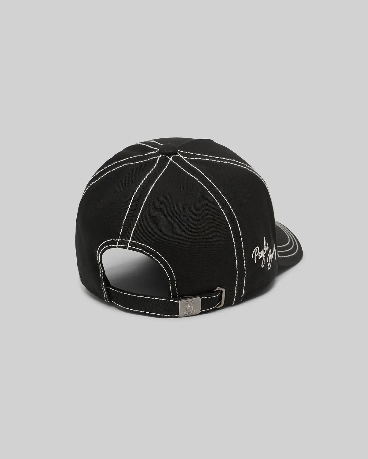 Mens Oscar Trucker Cap in black, featuring prominent white contrast stitching across panels and brim, an embroidered white Psycho Bunny script logo on the side, and a metal buckle with an engraved bunny skull. (4)