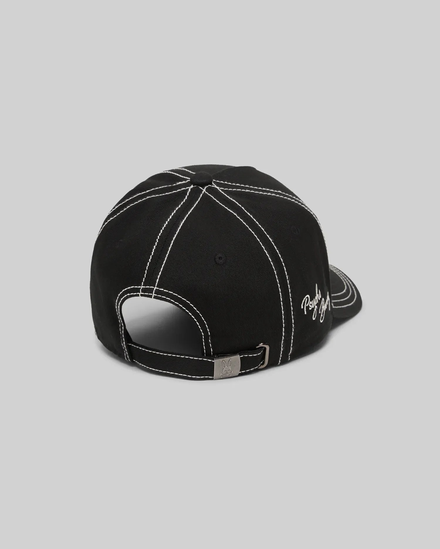 Mens Oscar Trucker Cap in black, featuring prominent white contrast stitching across panels and brim, an embroidered white Psycho Bunny script logo on the side, and a metal buckle with an engraved bunny skull. (4)