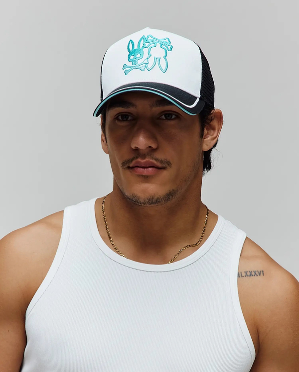 Mens Aram Trucker Cap featuring a white front panel, black mesh back, and a large teal embroidered Psycho Bunny skull logo. The brim is black with a white and teal stripe accent.