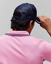 Pink pique polo shirt with navy and pink striped collar, paired with a navy blue mesh Mens Aram Trucker Cap featuring a white and pink striped brim. (3)