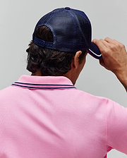 Pink pique polo shirt with navy and pink striped collar, paired with a navy blue mesh Mens Aram Trucker Cap featuring a white and pink striped brim. (3)
