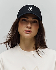 Black Mens Jimmy Baseball Cap with a prominent white embroidered Psycho Bunny skull and crossbones logo on the front, paired with a cream jersey knit t-shirt featuring a subtle textured graphic.
