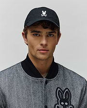 Mens Jimmy Baseball Cap in black with a white embroidered Psycho Bunny skull logo, paired with a black and white herringbone bomber jacket featuring a large embroidered Psycho Bunny skull patch.